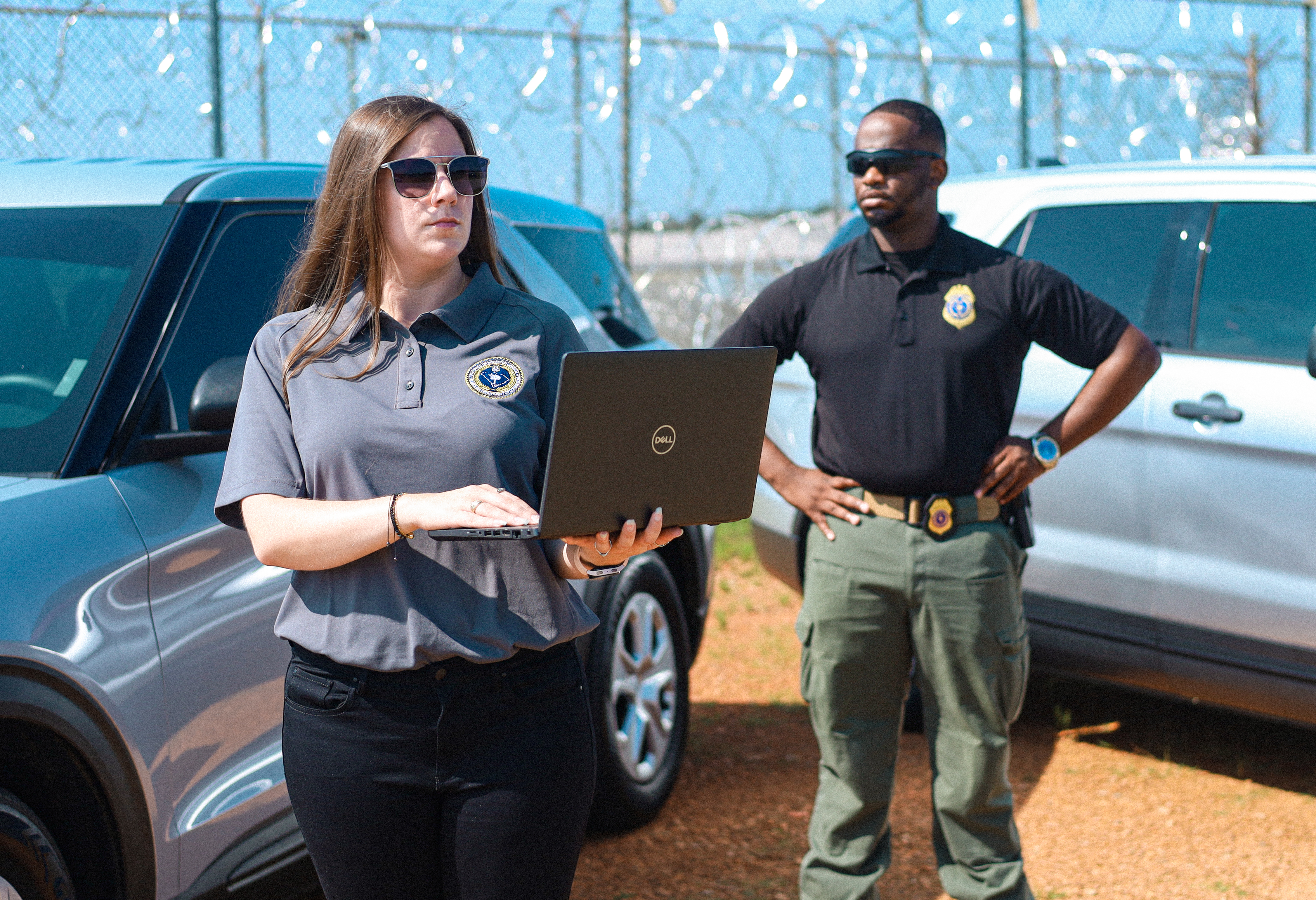 OIG Staff Holding a Laptop with another OIG Staff in the background of the photo posing looking off from the camera in the opposite direction.